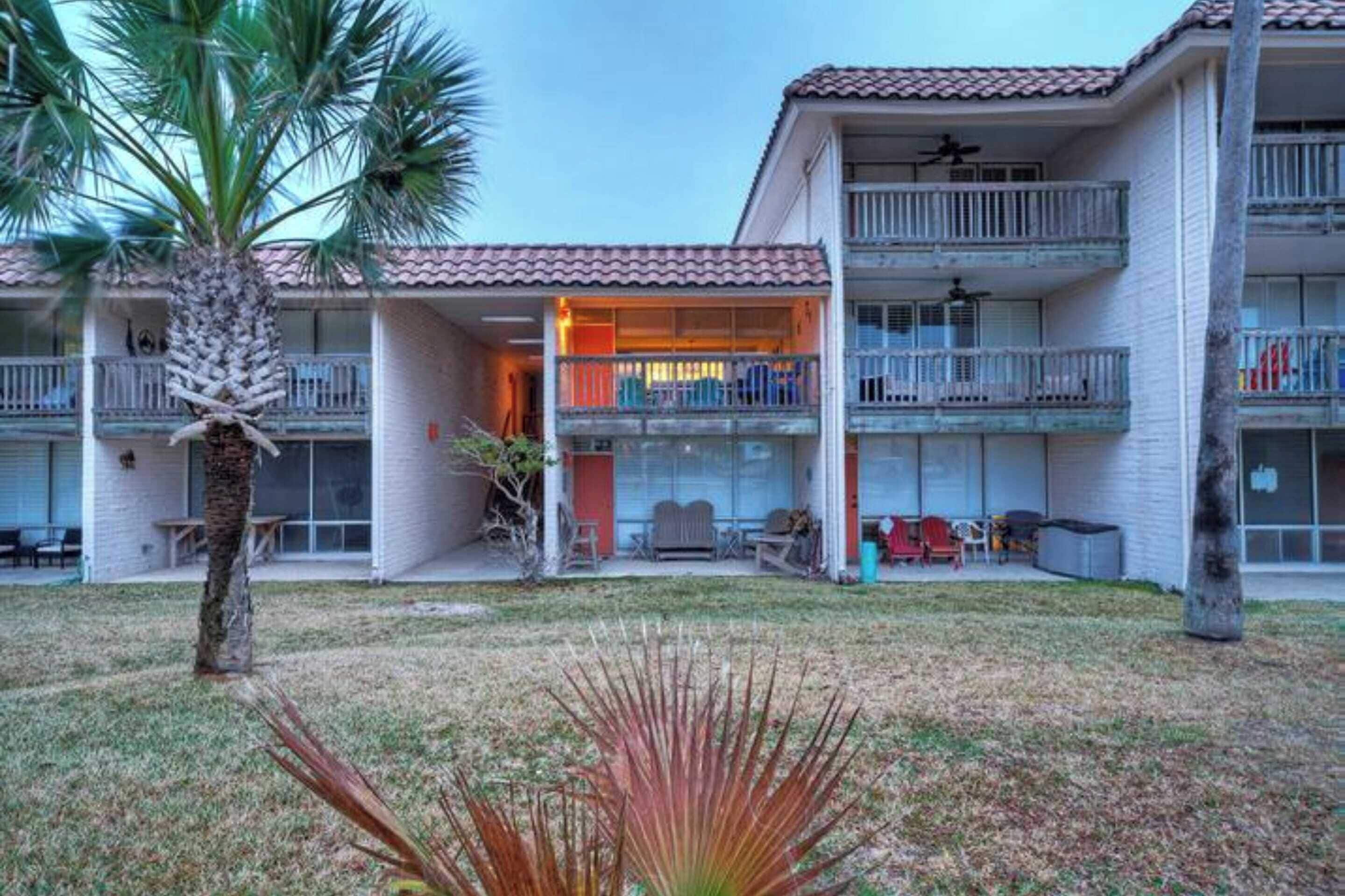 A multi-story building with balconies, a covered outdoor seating area, and a palm tree.