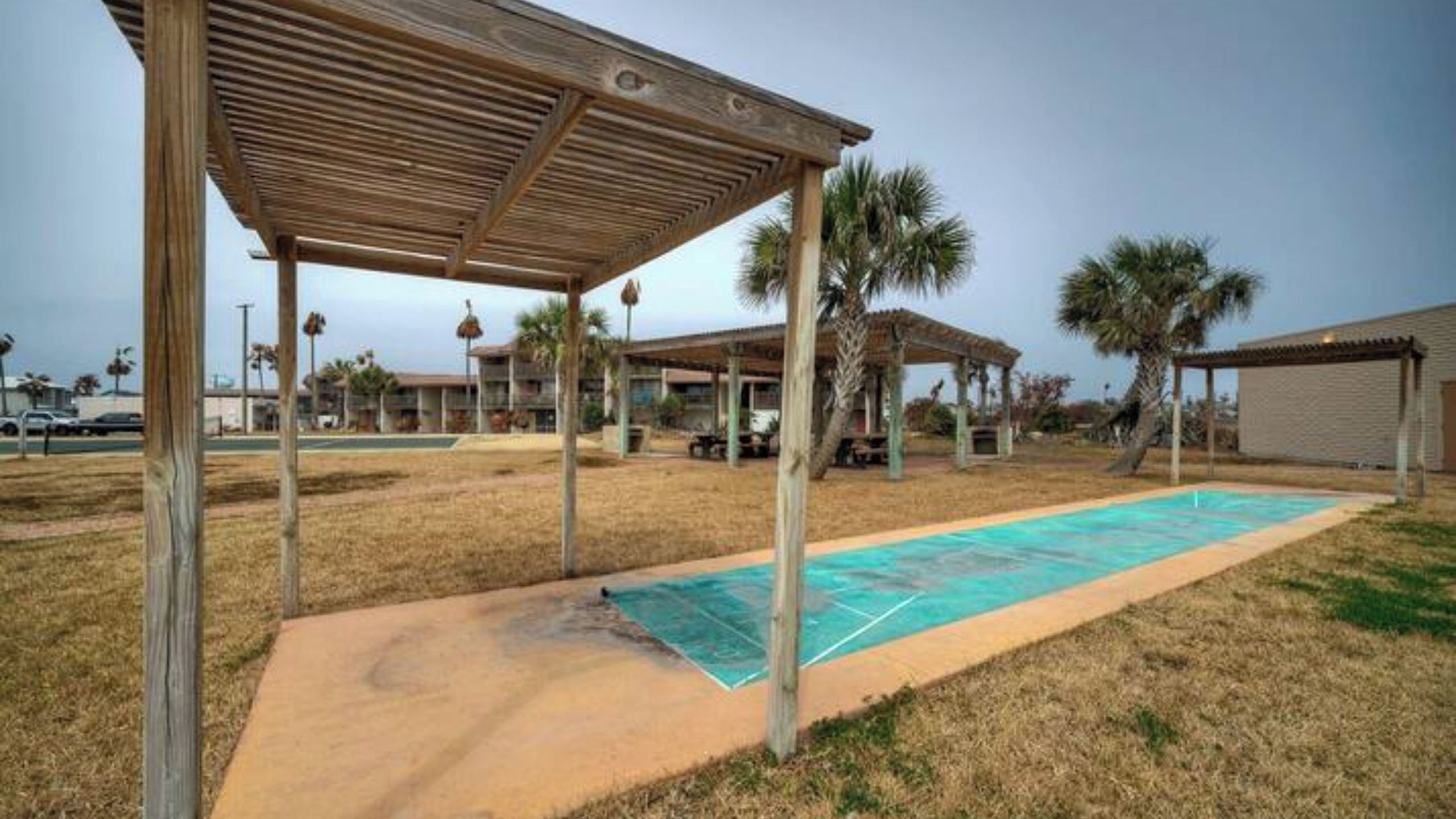 Un'area esterna coperta con piscina, palme e un edificio sullo sfondo.
