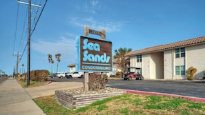 Une enseigne indiquant l’emplacement des appartements Sea Sands, avec une vue dégagée sur l’immeuble et sur le parking.