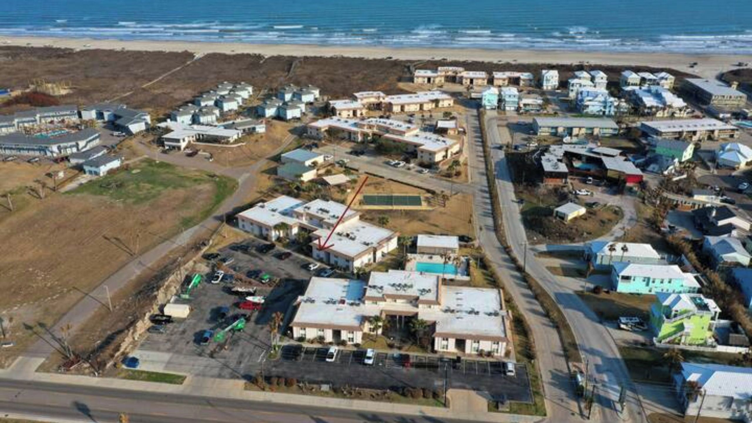 An aerial view of a coastal residential area with houses, a beach, and a road.