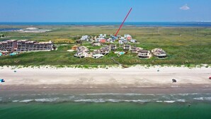 Luchtbeeld van een kustresort met meerdere gebouwen, een strand en een helder uitzicht op de oceaan.