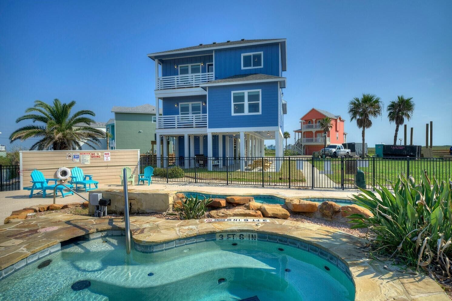 A two-story blue house with a swimming pool and lounge chairs.
