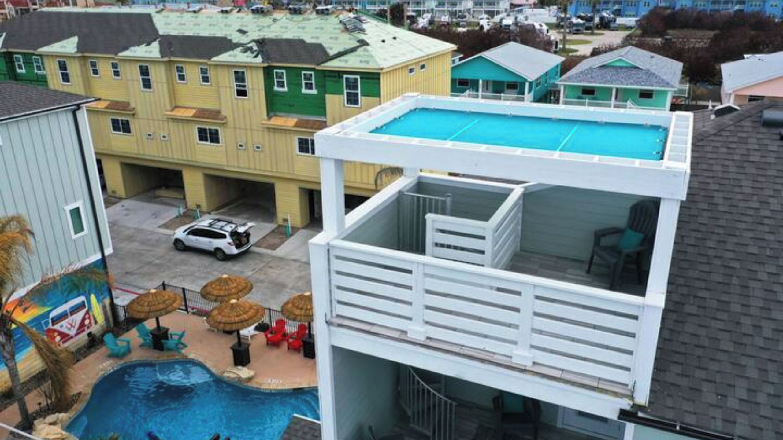 A residential building with a swimming pool, a covered patio area, and a car parked in front.