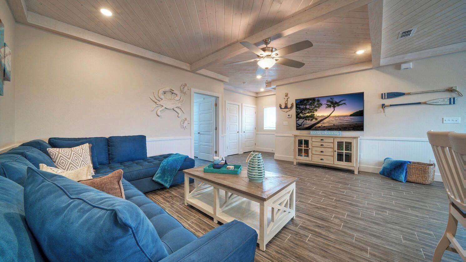 A spacious living room with a large blue sofa, a wooden coffee table, and a ceiling fan.