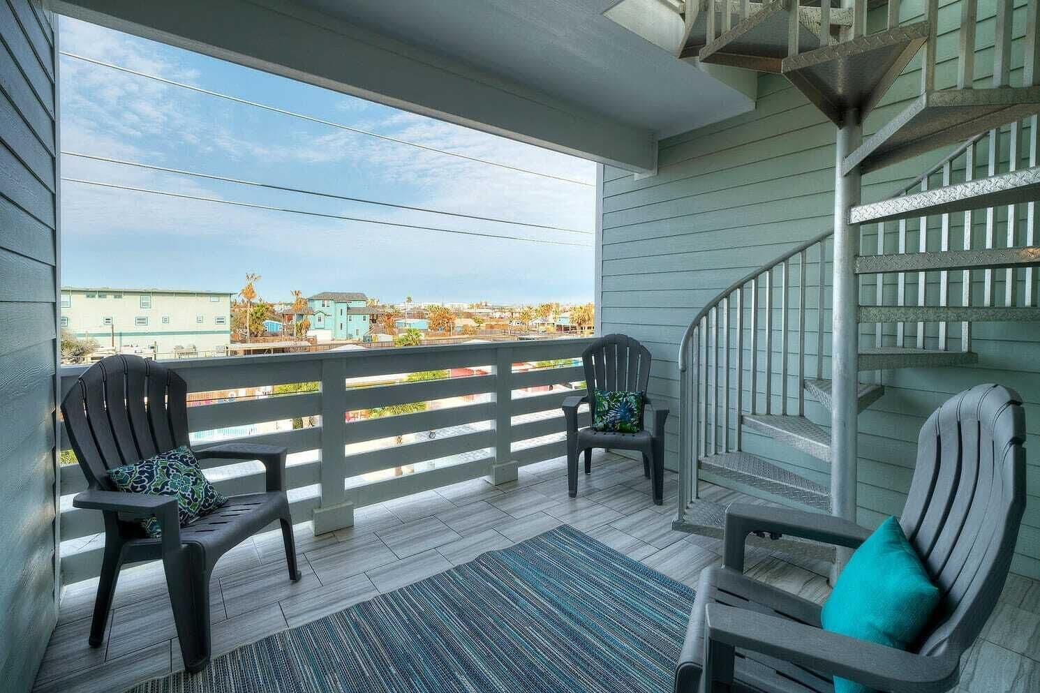 A covered porch with two Adirondack chairs, a small rug, and a staircase leading to an upper level.