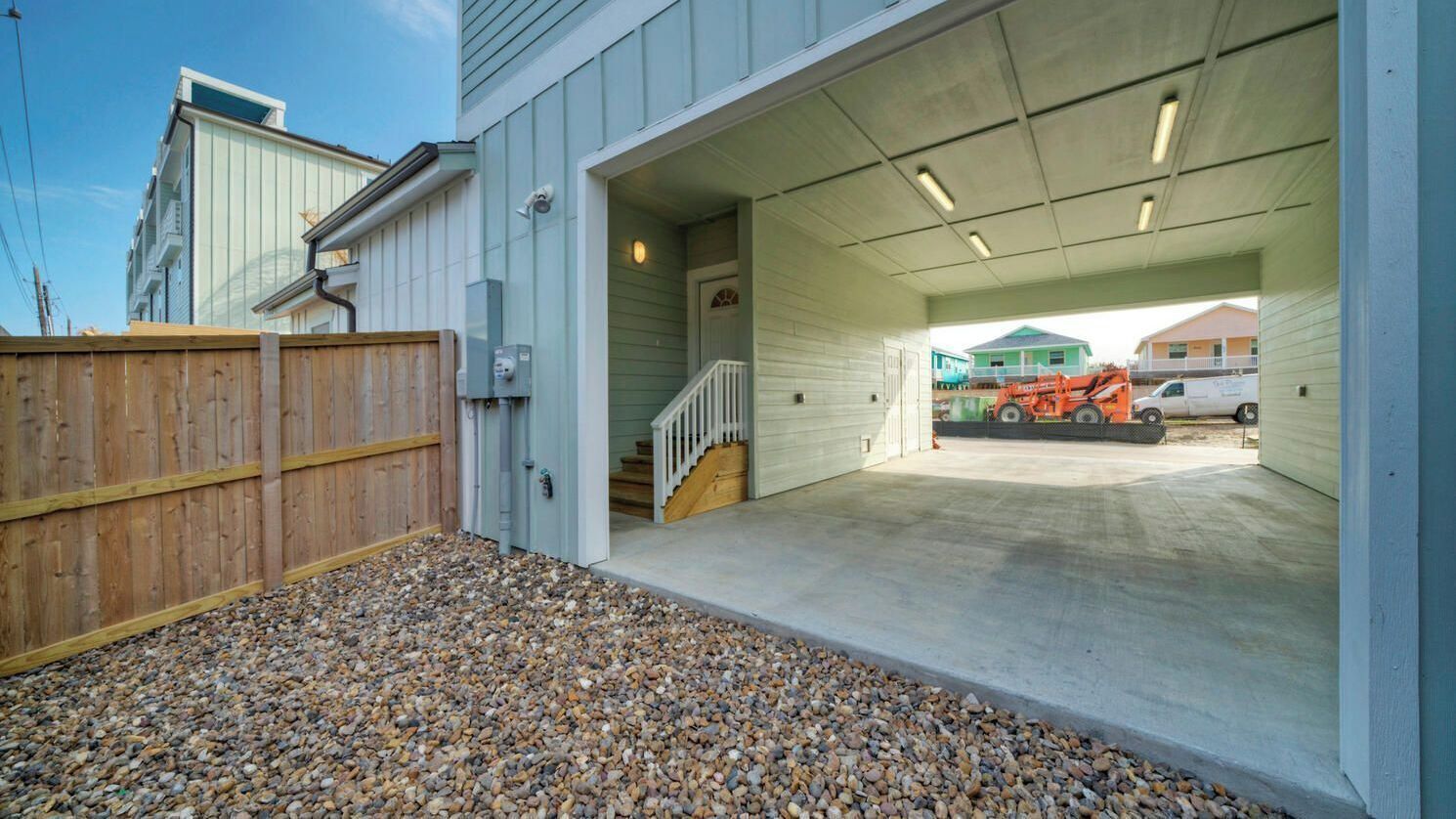 A covered garage entrance with a concrete floor, a wooden fence, and a gravel driveway.