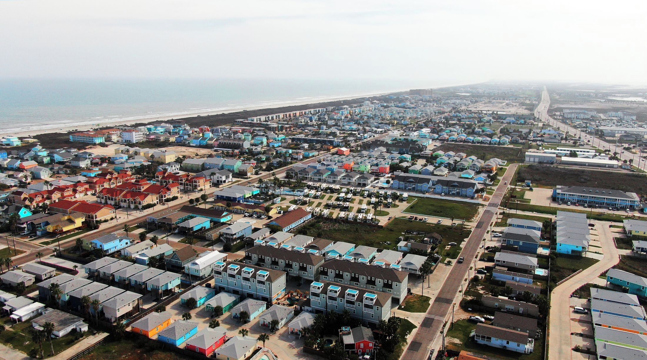An aerial view of a coastal residential area with houses, roads, and a beach.