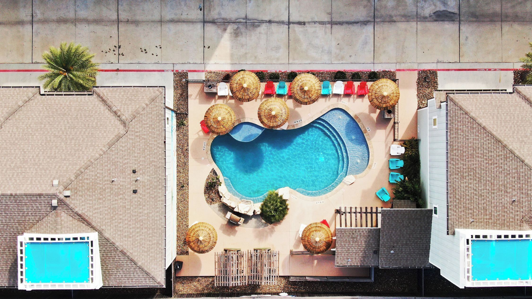 An aerial view of a pool area with a central pool, surrounding lounge chairs, and umbrellas.