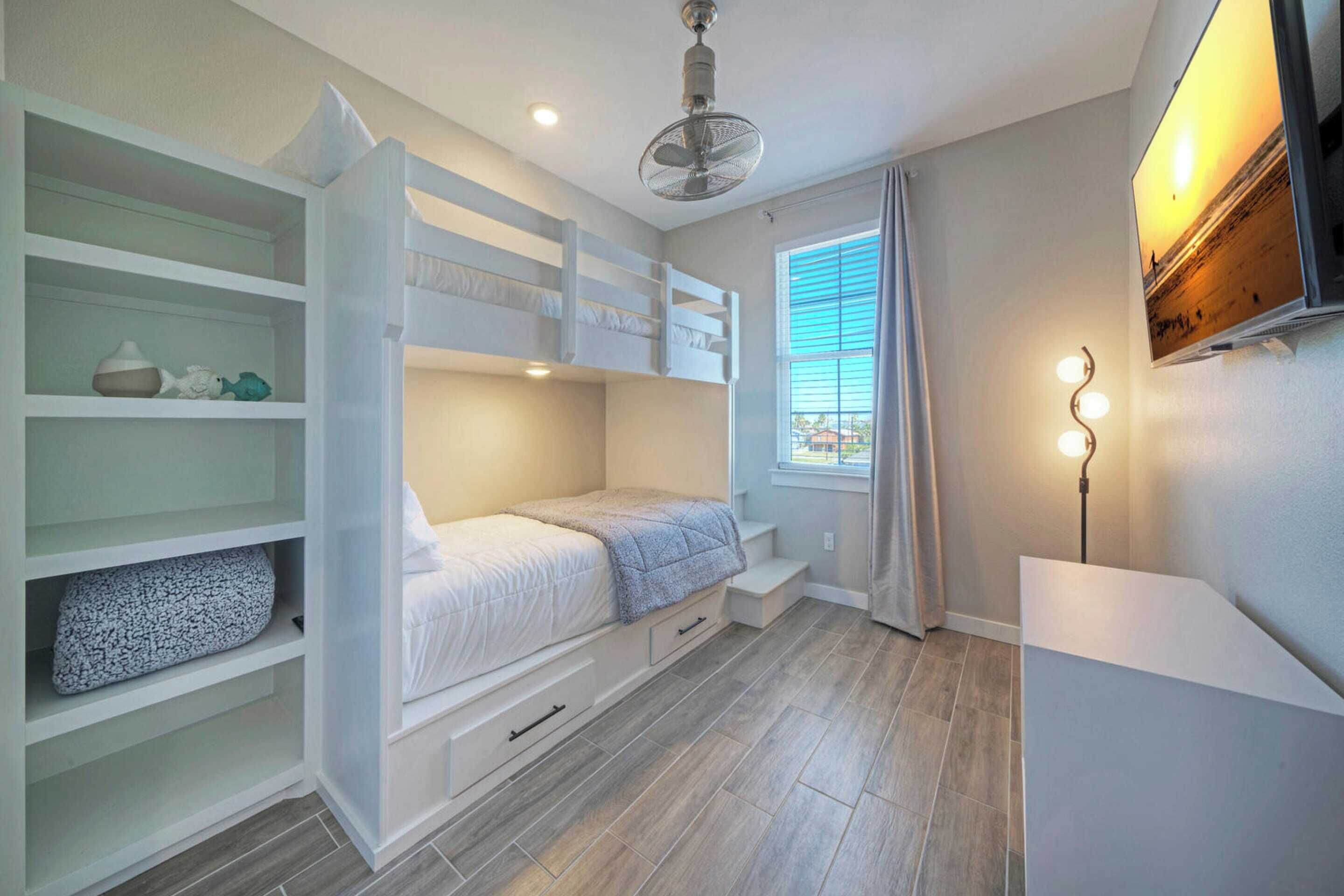 A bedroom with a bunk bed, a desk, a lamp, and a window with curtains.