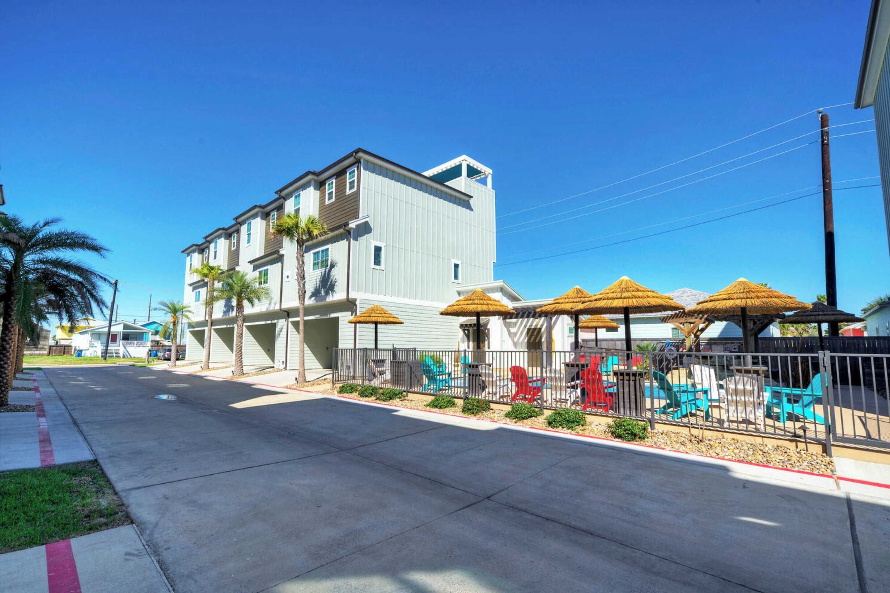 A two-story building with a flat roof, a covered outdoor seating area with umbrellas, and a paved sidewalk.