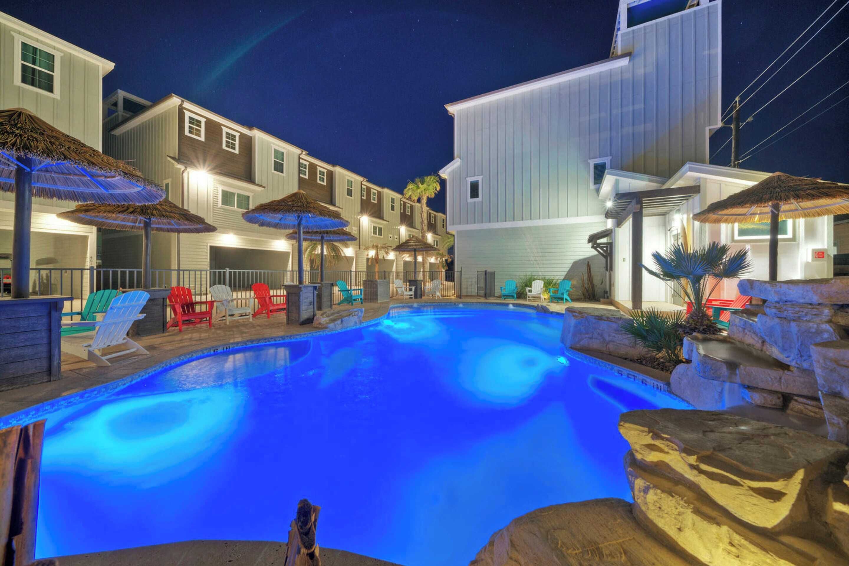 A swimming pool with lounge chairs and umbrellas, surrounded by buildings with a light-colored exterior.