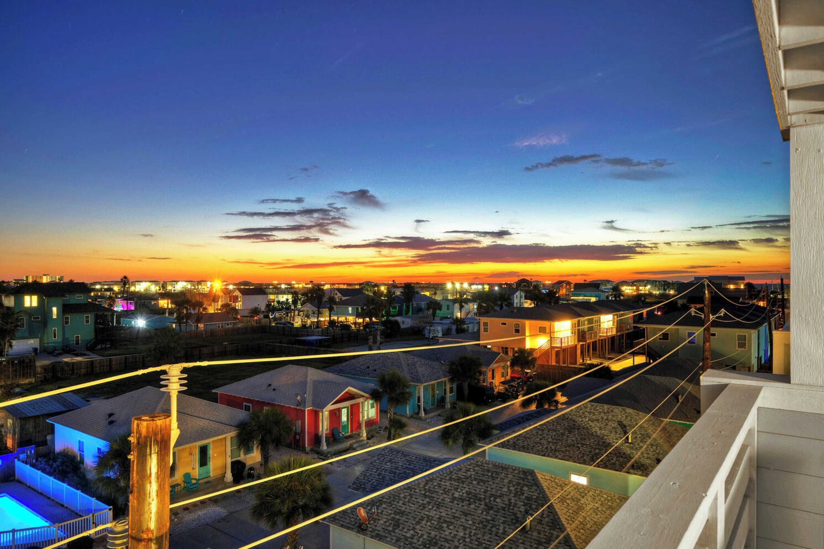 Vista al tramonto da un balcone che si affaccia su una zona residenziale con case e una piscina.