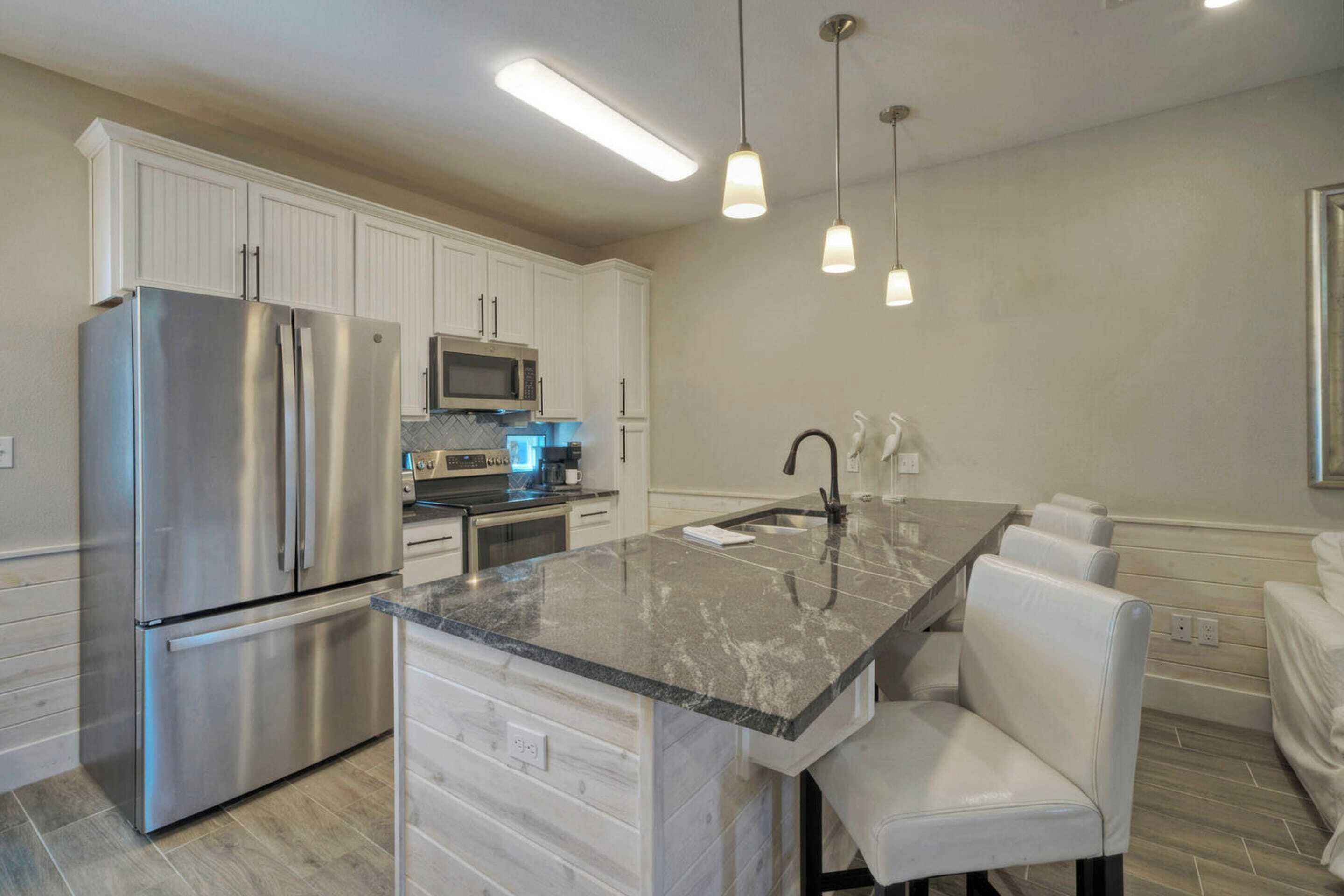 A modern kitchen with white cabinets, stainless steel appliances, a granite countertop, and pendant lighting.