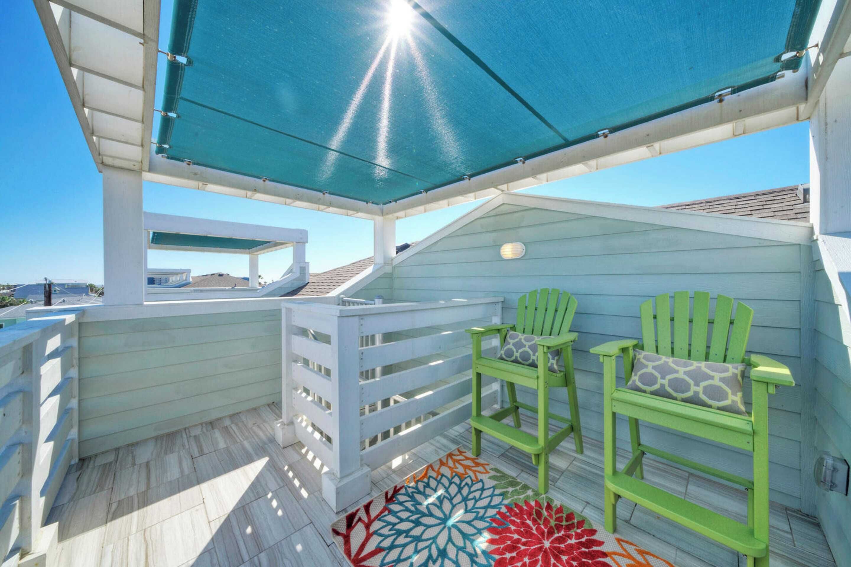 A covered outdoor deck with two green chairs and a colorful rug.