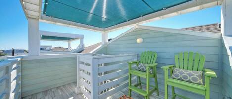A covered outdoor deck with two green chairs and a colorful rug.