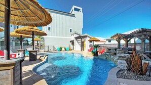 A swimming pool with a curved edge, surrounded by lounge chairs and umbrellas.