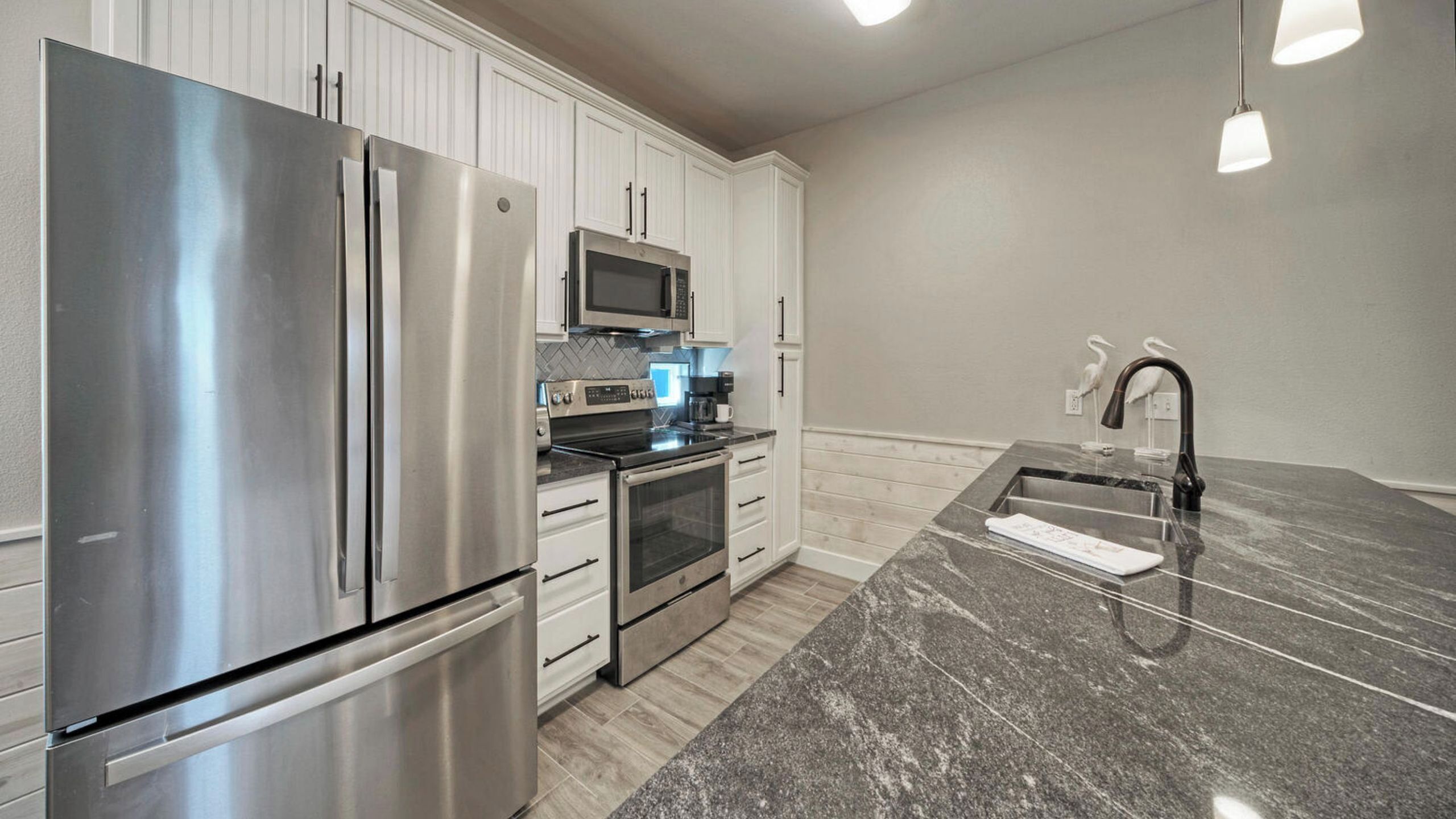 A modern kitchen with stainless steel appliances, white cabinetry, and a granite countertop.