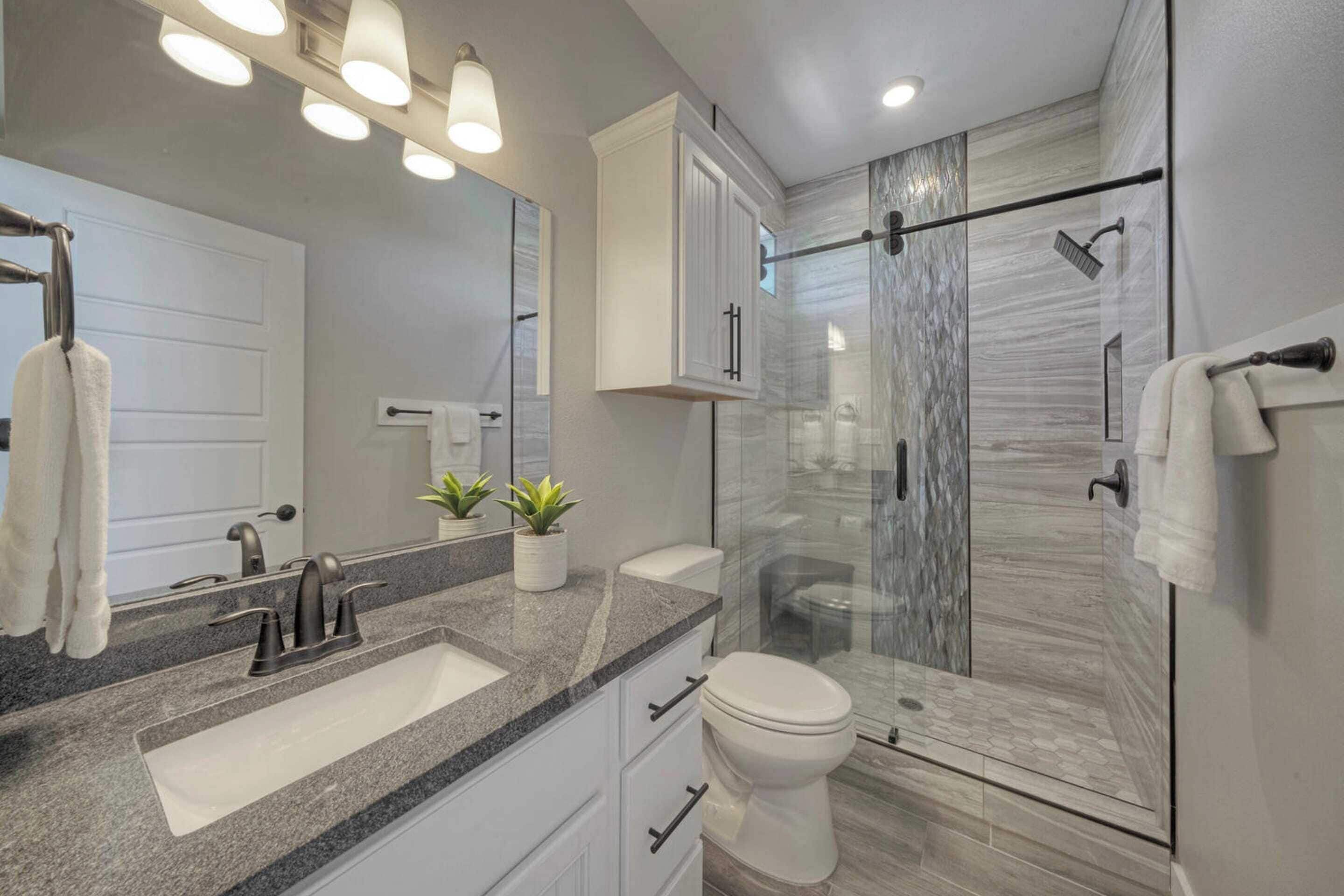 A modern bathroom with a granite countertop sink, a white toilet, and a glass-enclosed shower.
