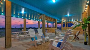 An outdoor patio with Adirondack chairs and a view of the sunset over water. - Outdoor Lounge w/ Bar Swing Seats, Near Nature Preserve Blutopia by Avantstay (Port Aransas)