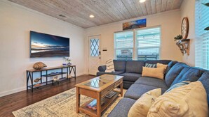 A cozy living room with a wooden ceiling, a large painting, a sofa, a coffee table, and a bookshelf. - Port A Hideaway by Avantstay Private Pool (Port Aransas)