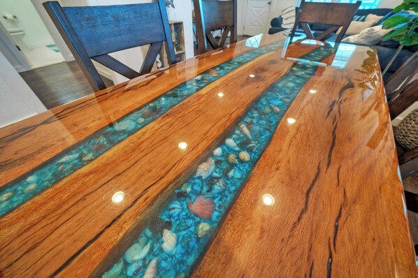 A wooden dining table with a glass top featuring a blue and white mosaic pattern. - Port A Hideaway by Avantstay Private Pool (Port Aransas)