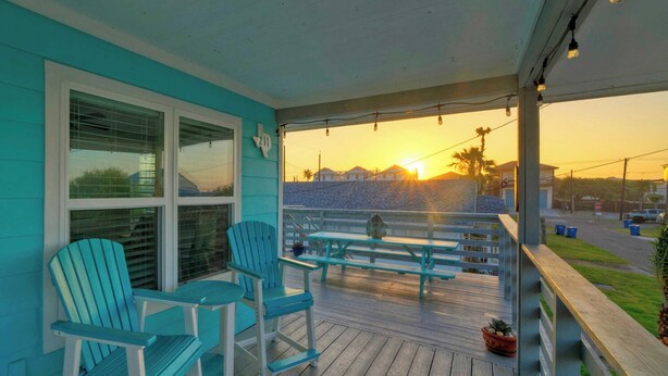 Portico con due poltrone Adirondack e un tavolo, vista su una spiaggia al tramonto.