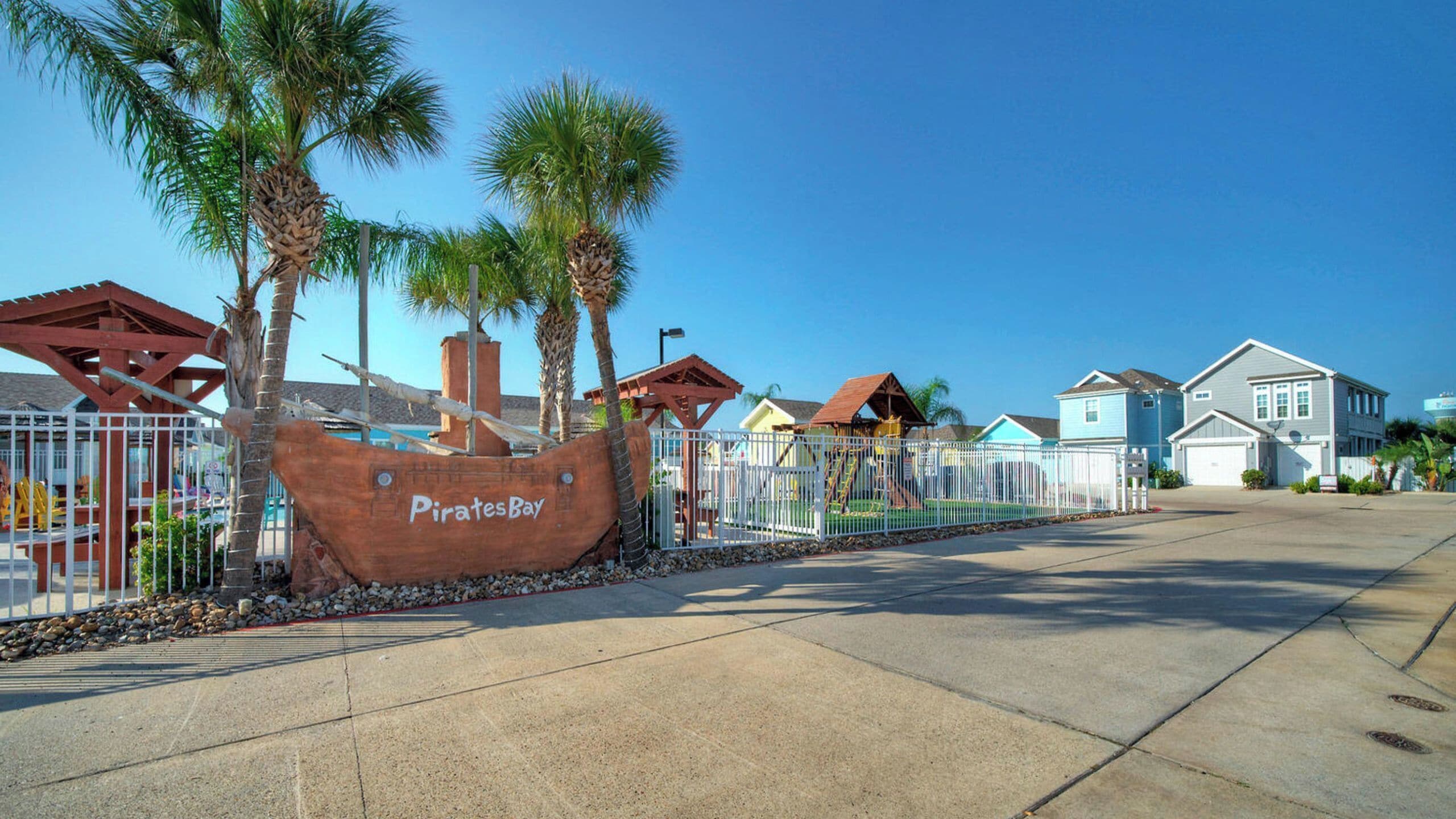 A coastal area with a large wooden pirate ship sign, palm trees, and residential houses.