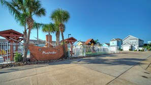 Une zone côtière avec un grand panneau en bois représentant un navire de pirates, des palmiers et des maisons d’habitation.