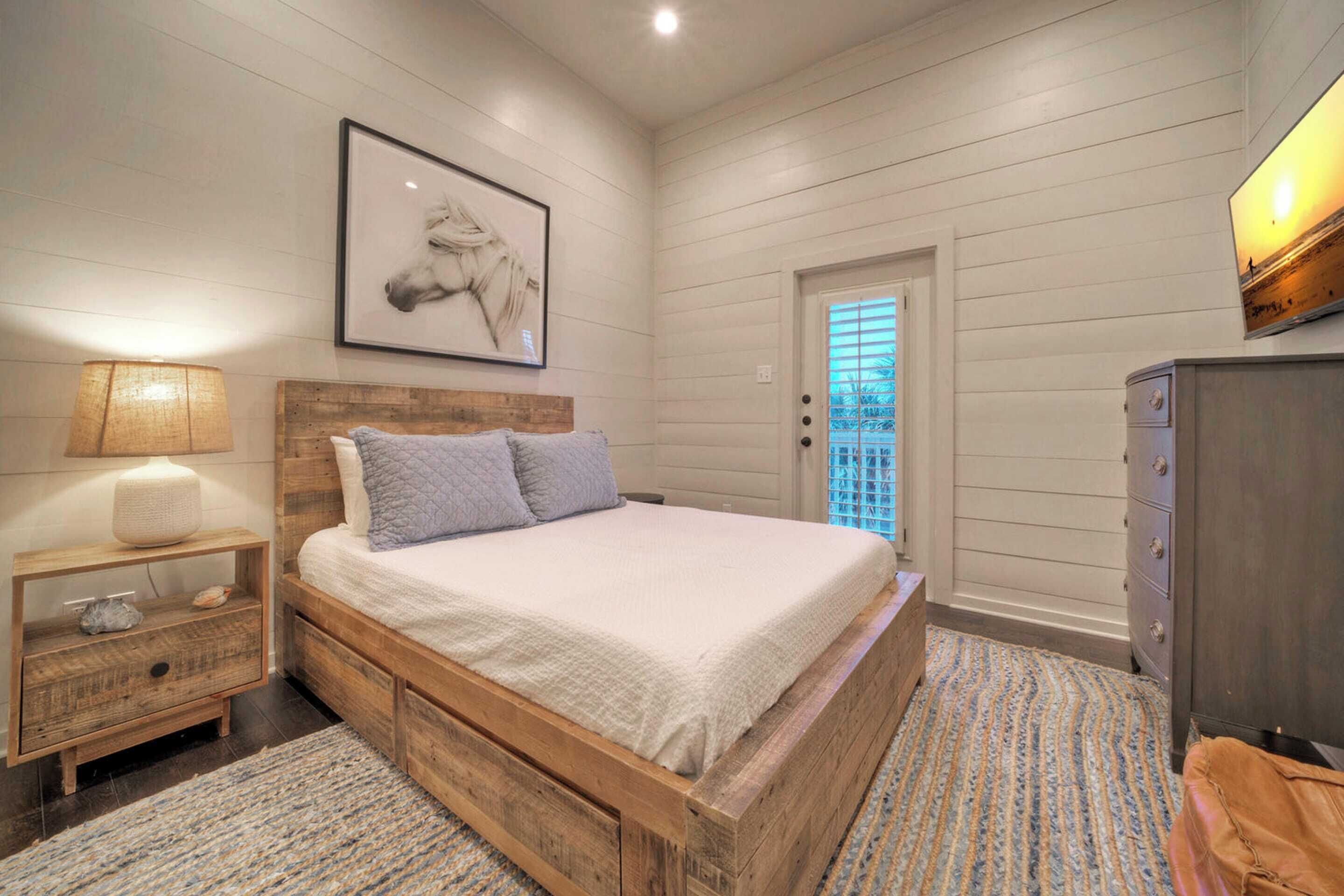 A bedroom with a wooden bed, a nightstand, a dresser, and a framed picture on the wall.