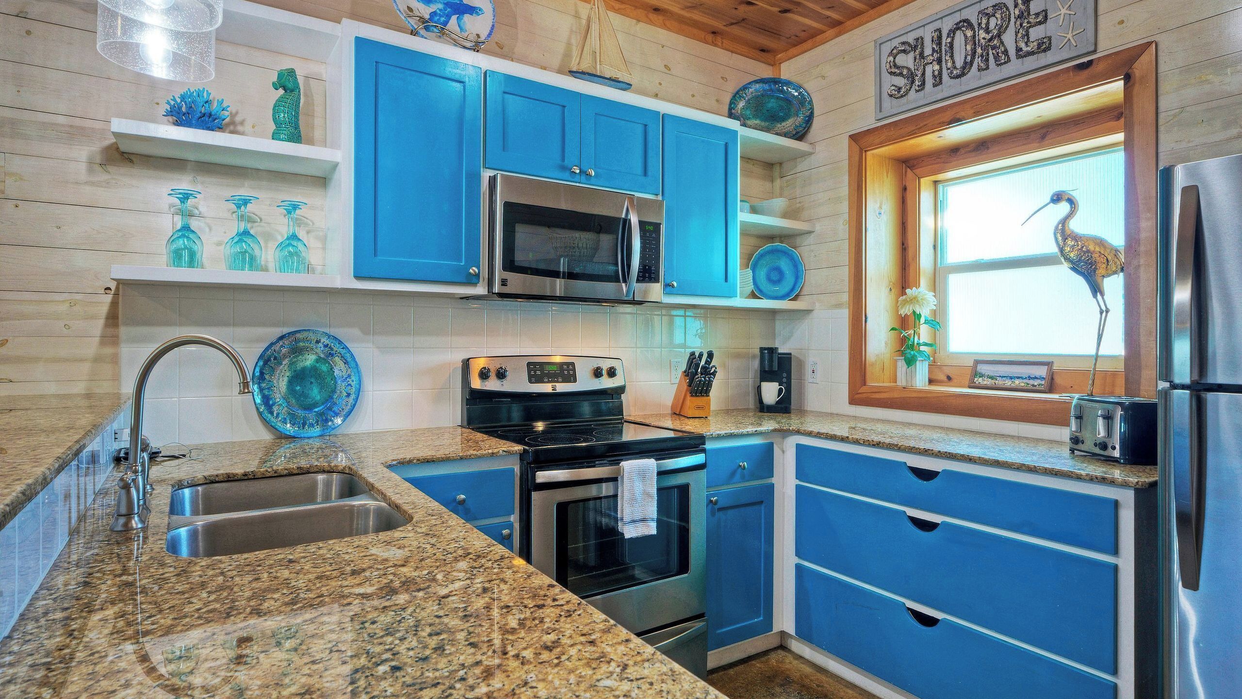 A kitchen with blue cabinets, a microwave, a stove, and a sink.