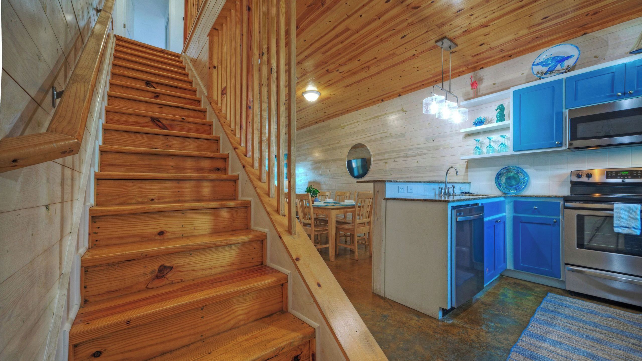 A wooden staircase leading to a dining area with a kitchen featuring blue cabinets and stainless steel appliances.