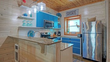 Una cocina con armarios azules, un refrigerador de acero inoxidable y una ventana con vista a la playa.