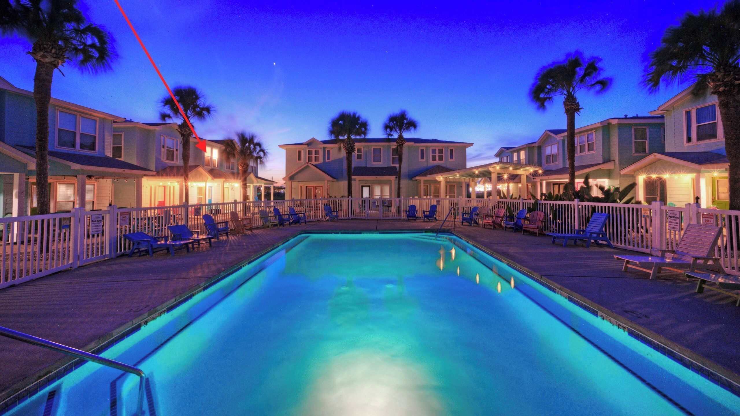 A swimming pool with lounge chairs and a row of houses in the background.
