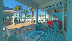A covered outdoor area with seating, a patterned rug, and a view of palm trees and buildings. - Pool, Patio, Blocks to the Beach Golf Cart Zone Daiquiri Daze by Avantstay (Port Aransas)