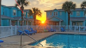 A pool area with lounge chairs and a sunset in the background. - Pool, Patio, Blocks to the Beach Golf Cart Zone Daiquiri Daze by Avantstay (Port Aransas)