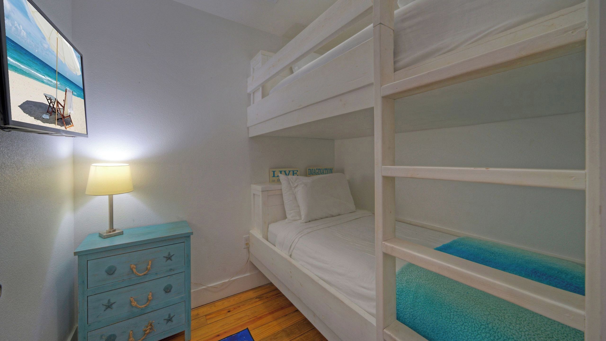 A bedroom with bunk beds, a dresser with star-shaped handles, a lamp, and a framed picture of a beach scene.