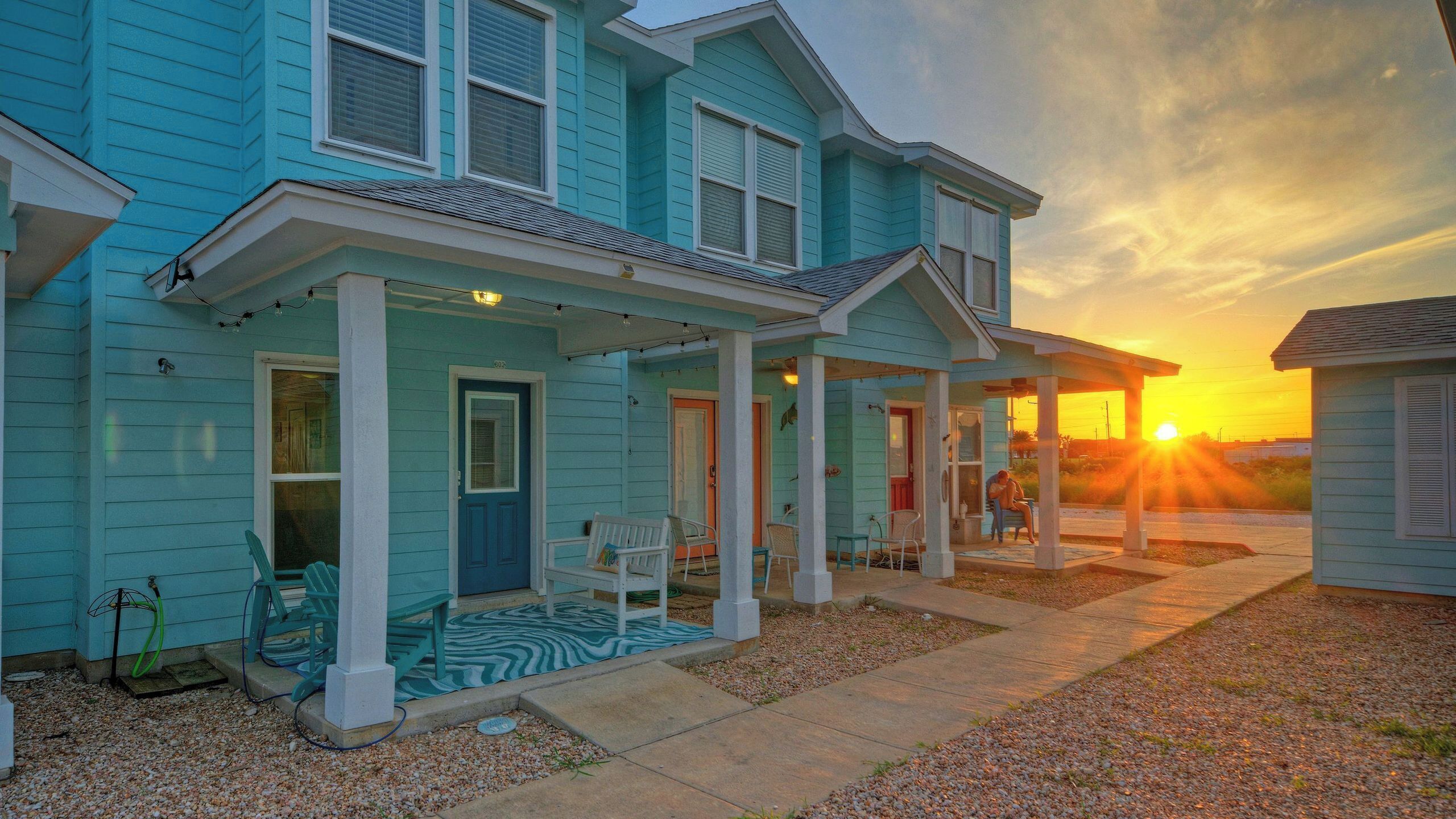 A two-story house with a porch, a door, and a small outdoor seating area.
