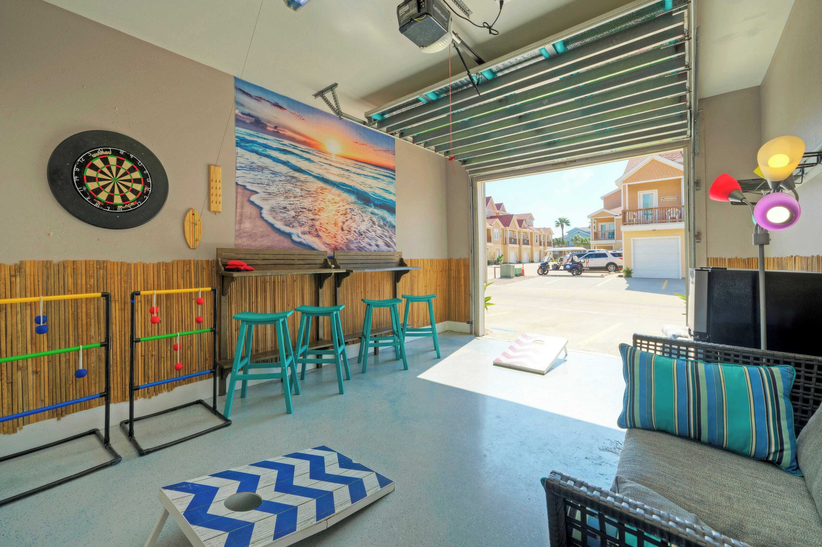 A room with a dartboard, a foosball table, and a foosball table with a blue and white chevron pattern. There are three green stools and a couch with a striped pillow.