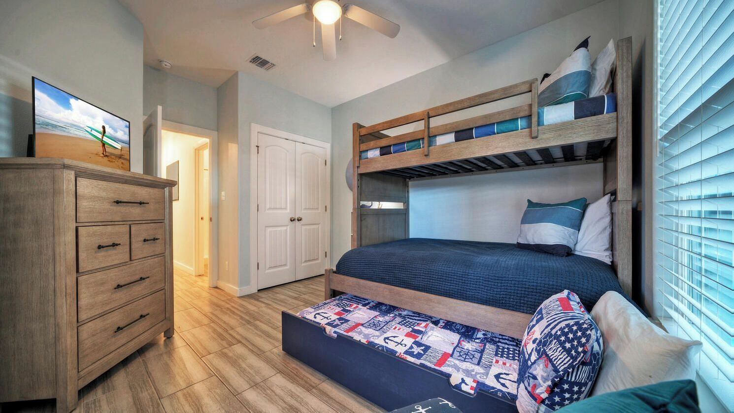 Un letto a castello con materasso trapuntato, una cassettiera in legno e una ventola a soffitto.