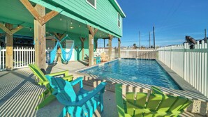 Un espace piscine doté d’une terrasse en bois, d’un hamac et de chaises colorées.
