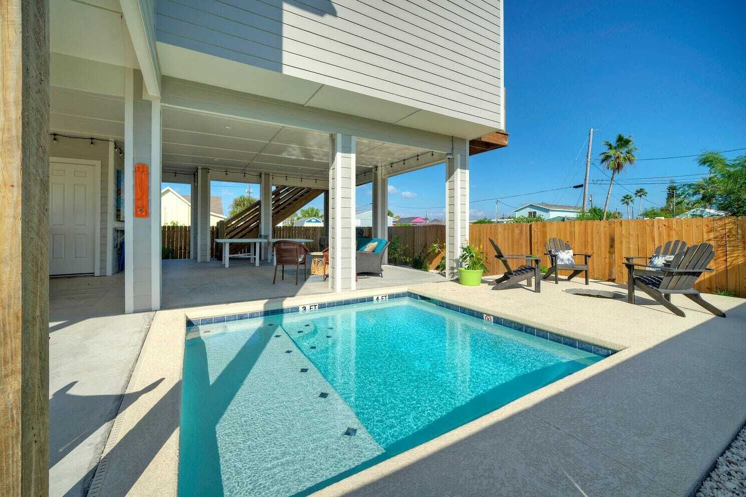 Une piscine avec un patio couvert, des meubles d’extérieur et une clôture en bois en arrière-plan.