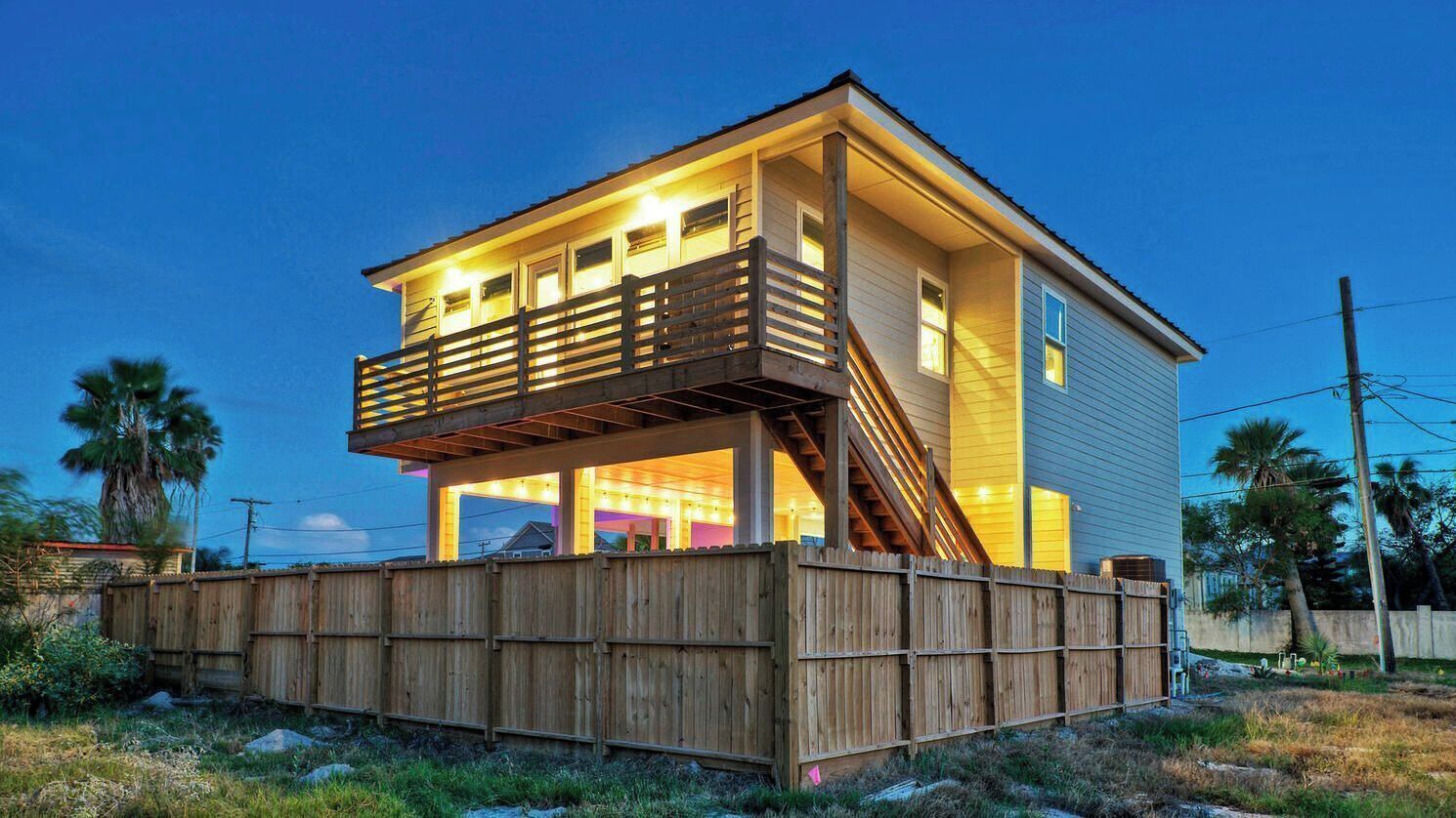 Une maison à deux étages avec un balcon, une clôture en bois et un ciel dégagé.