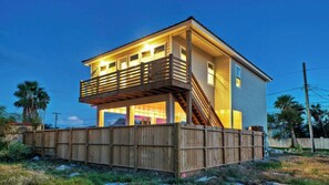 A two-story house with a balcony, a wooden fence, and a clear sky. - Monte Kristeaux by Avantstay Private Pool (Port Aransas)