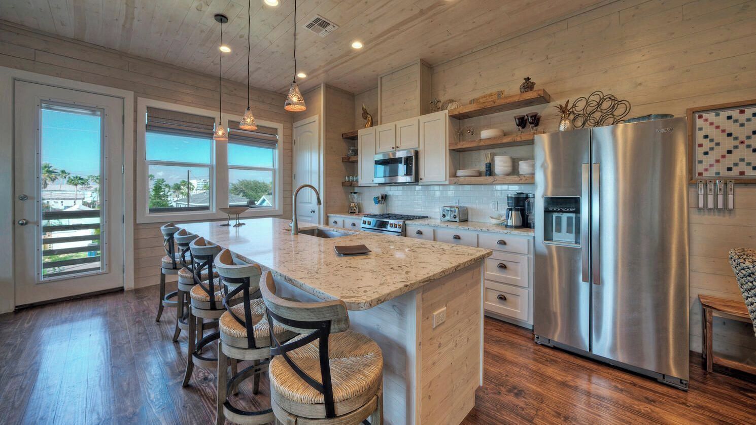A kitchen with a large island, stainless steel appliances, and a view through the sliding glass doors.