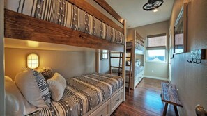 Un dormitorio con literas, una lámpara de noche, vigas de madera y vistas de la ciudad a través de una ventana.