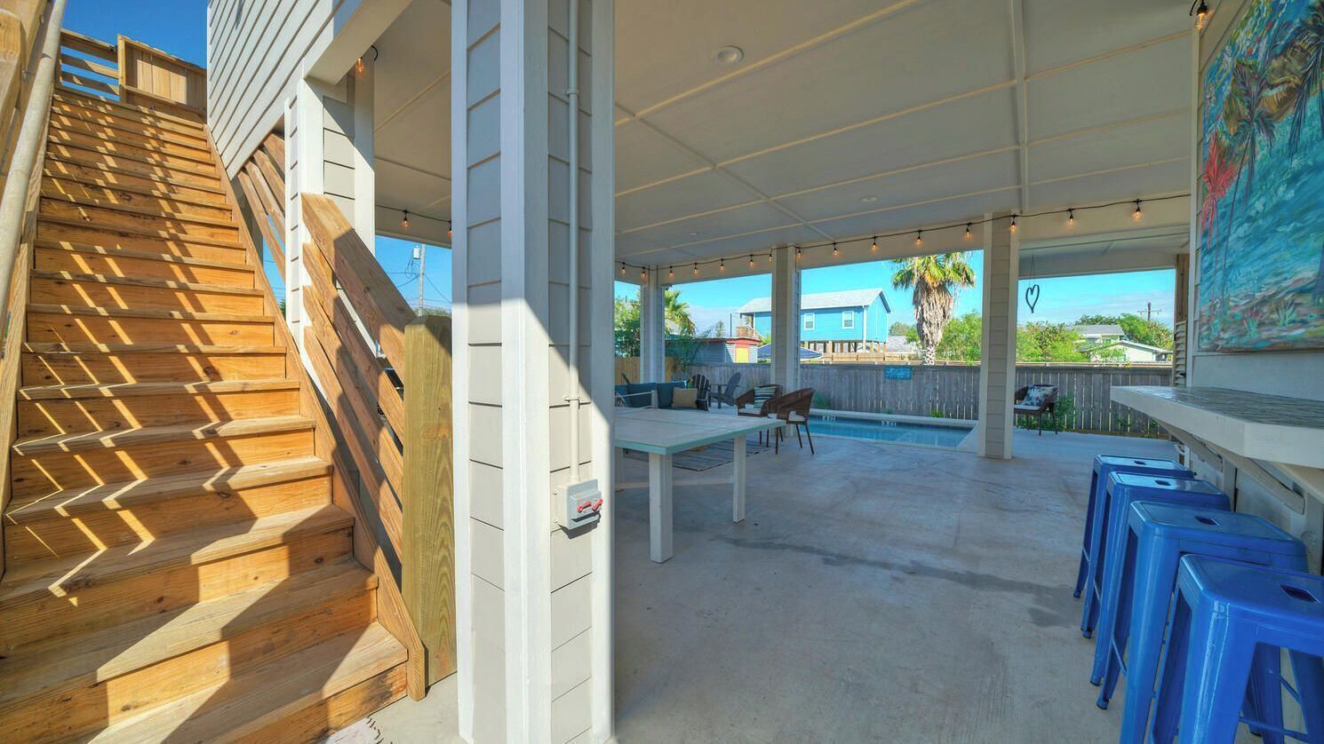 Un espacio al aire libre techado con una escalera de madera, una piscina y taburetes de plástico azul.