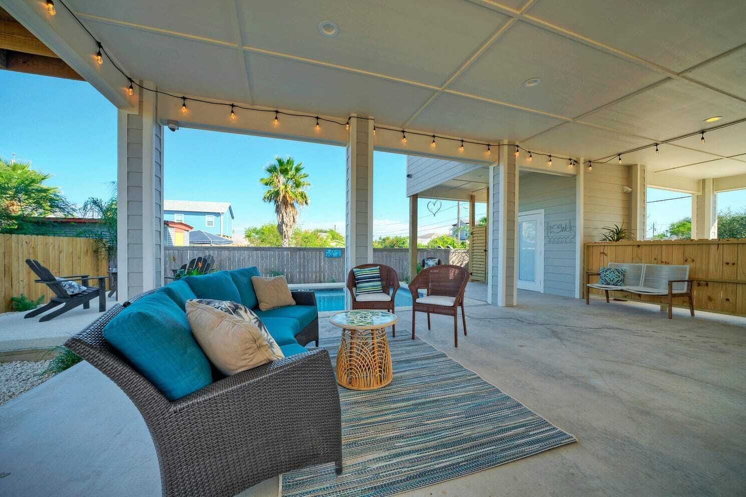 A covered patio area with a wicker sofa, two chairs, a small round table, and a striped rug.
