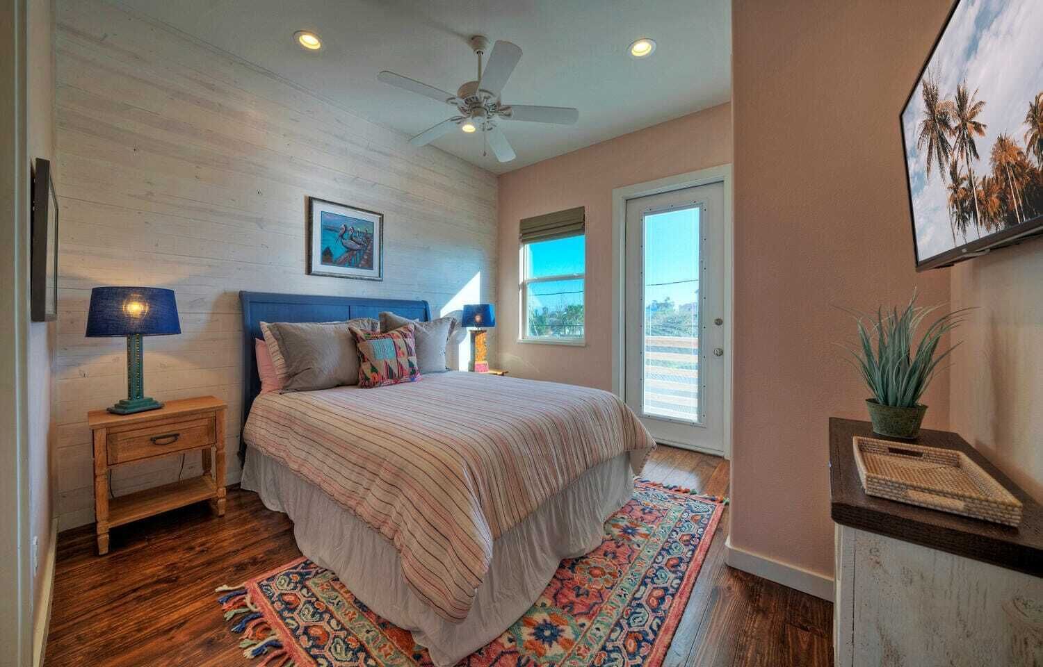 Une chambre à coucher avec un lit, un ventilateur de plafond, une fenêtre, une porte et un téléviseur fixé au mur.