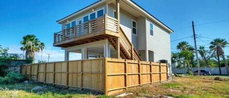 A two-story house with a wooden deck and a staircase leading to the upper floor.