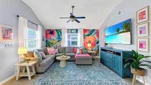 A living room with a sofa, ottoman, coffee table, and a TV. - Totally Beachin by Avantstay Private Heated Pool, Hot Tub + Fire Pit! (Port Aransas)